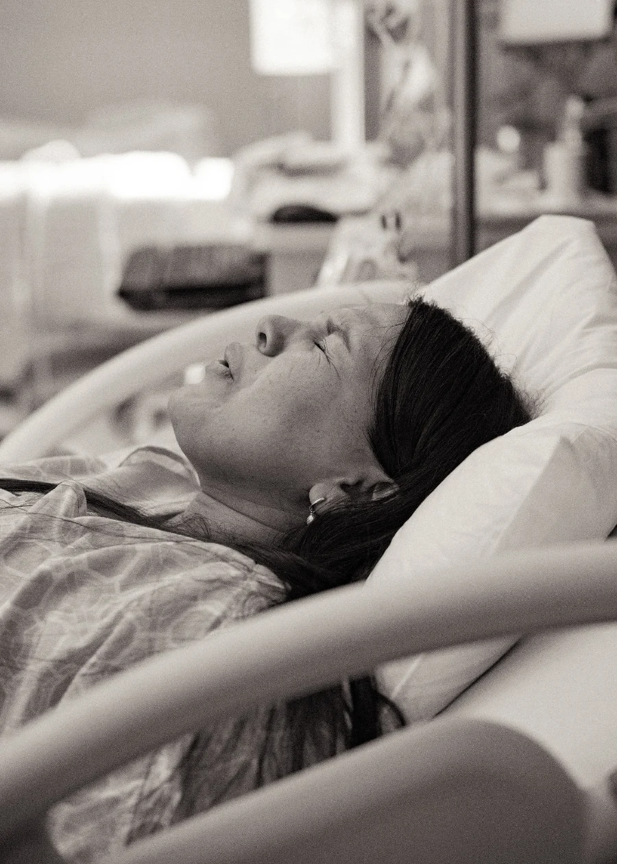 A laboring mother in a hospital bed breathes through a contraction with her eyes closed, in black and white