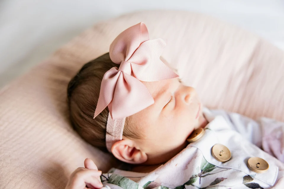 A sleeping newborn girl in a pink bow and a floral outfit with wooden buttons